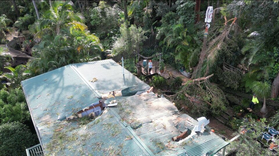 Aerial view of a damaged house in Avalon after severe weather, showing fallen tree branches and debris on the roof, highlighting the need for urgent tree removal services by Dixons Trees.
