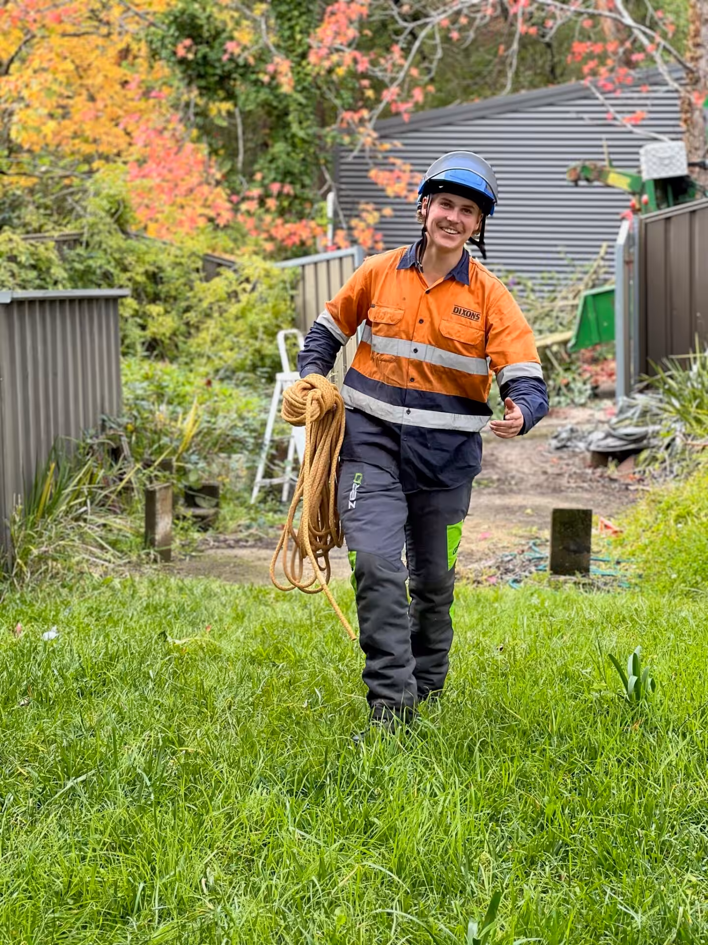 Worker in helmet carrying rope in backyard garden