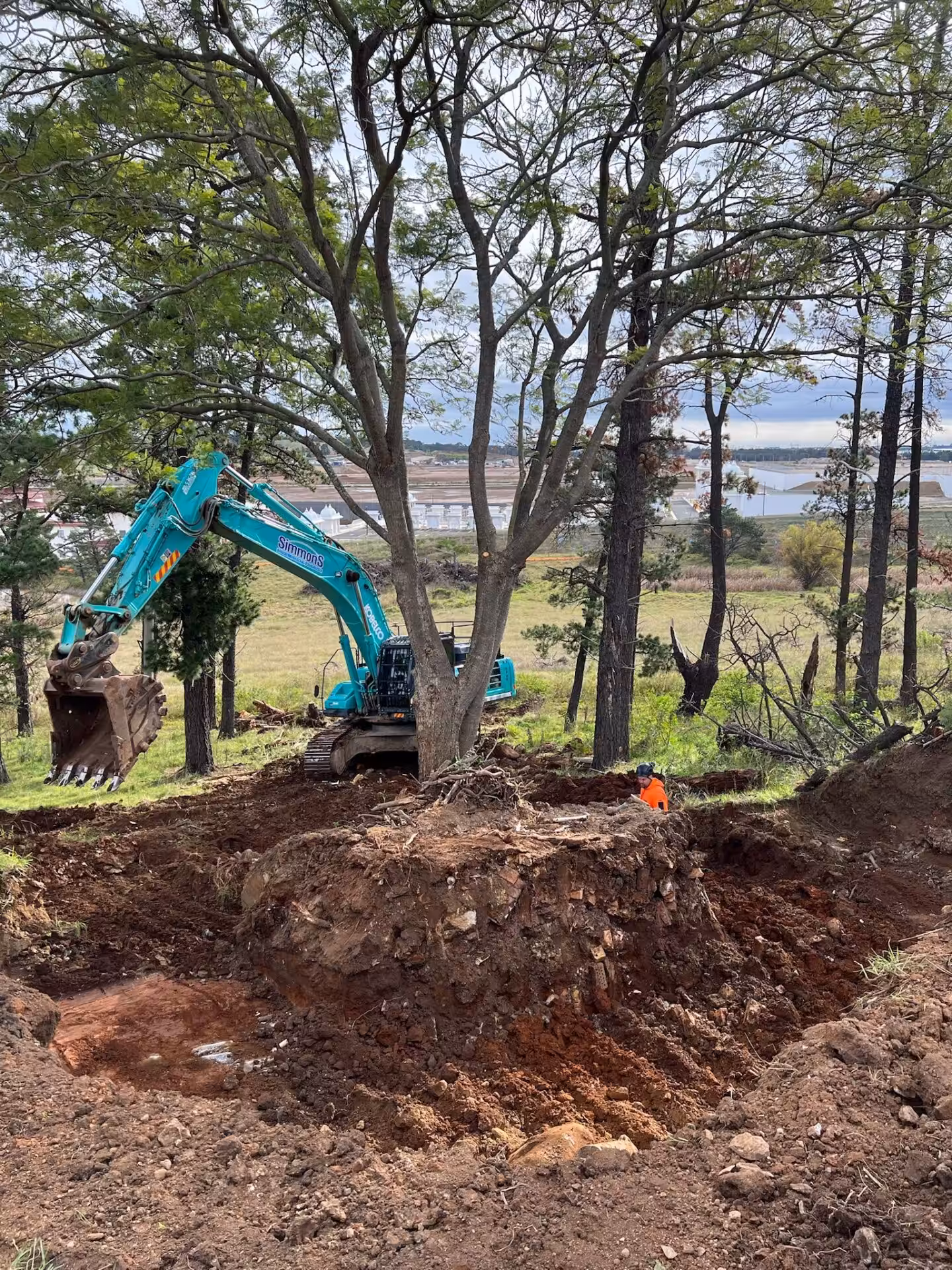 Excavator digging near trees on hillside construction site